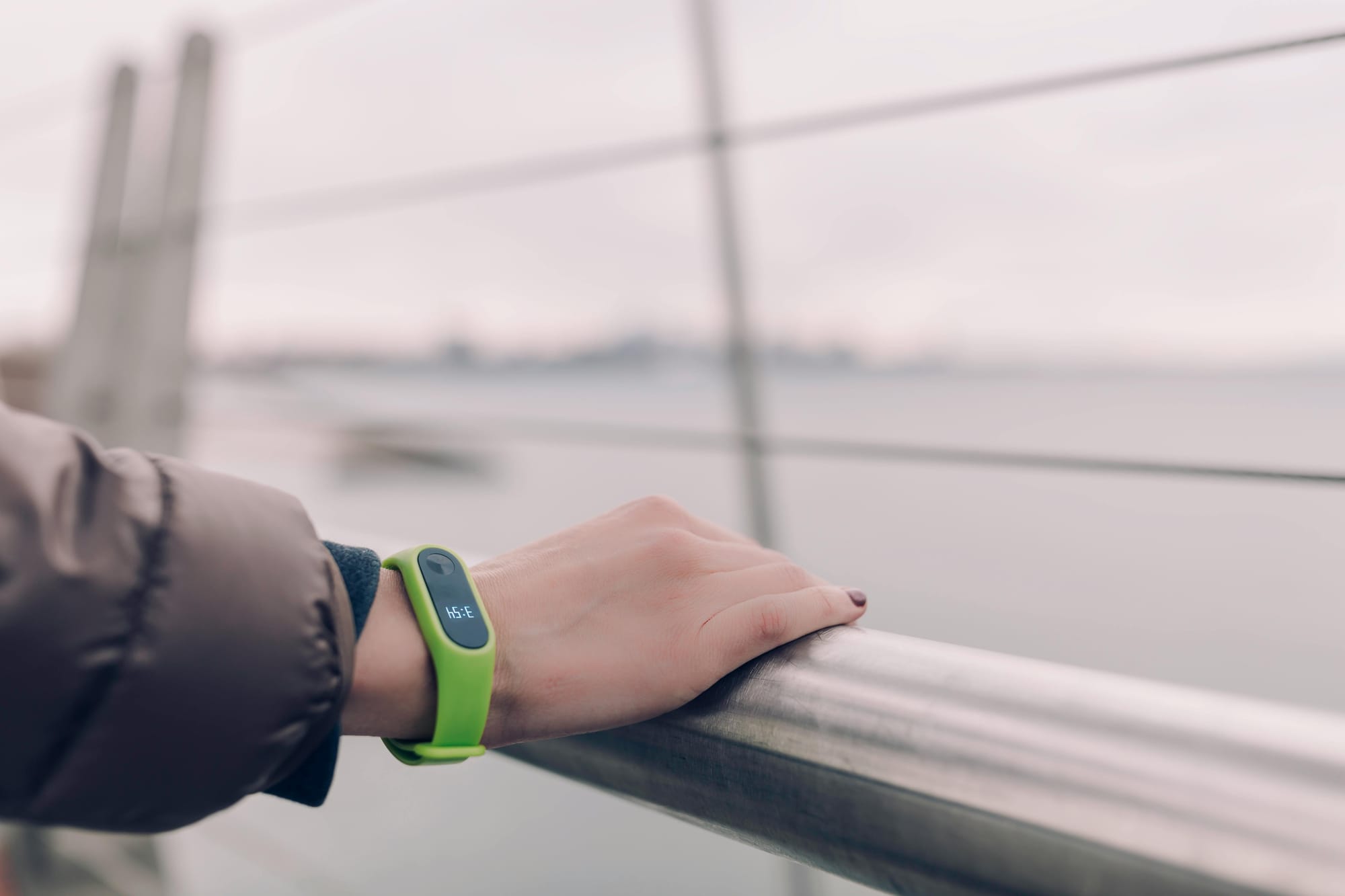Closeup of a woman's hand resting on a guardrail. She is wearing a bright yellow fitness tracker on her wrist.