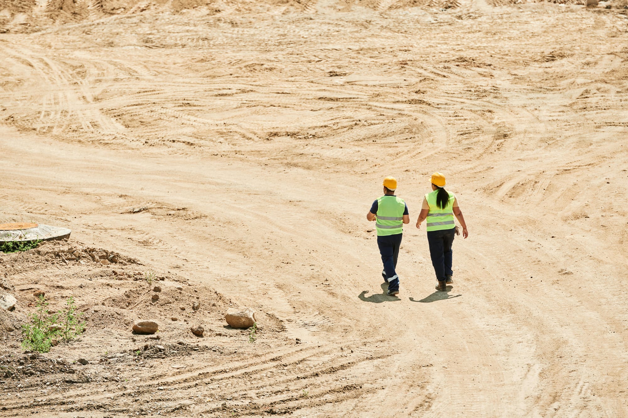 Two workers walking together across large dirt area