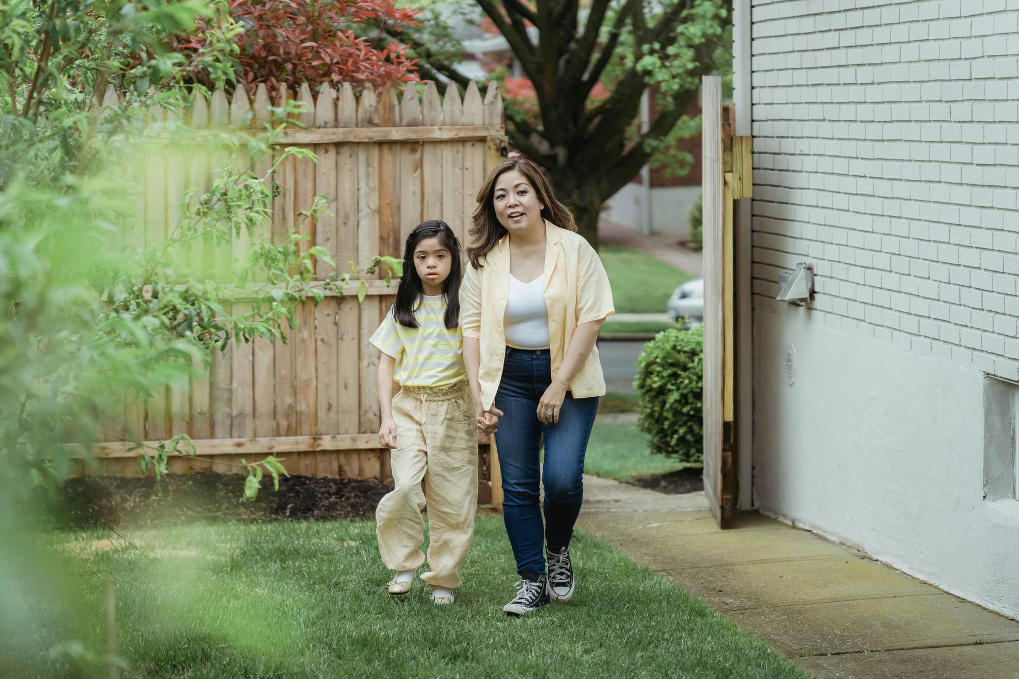 A mom and daughter walking through the gate into their grassy backyard.