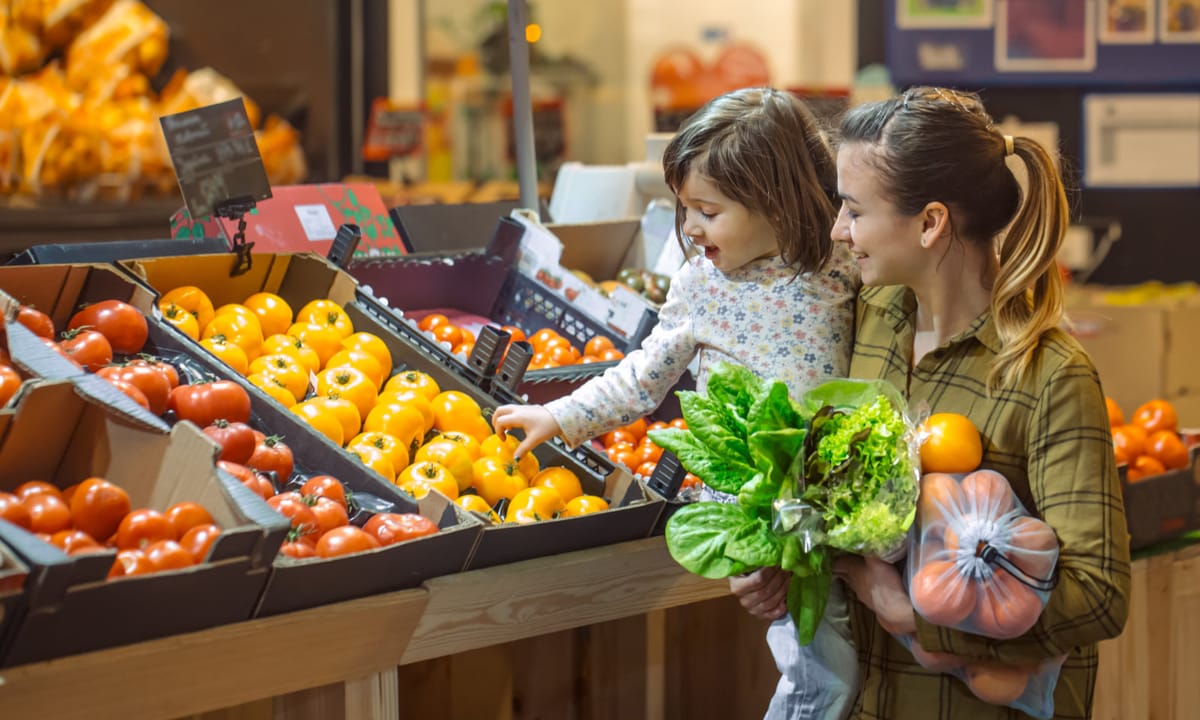 A happy mother buying fresh produce with her toddler.