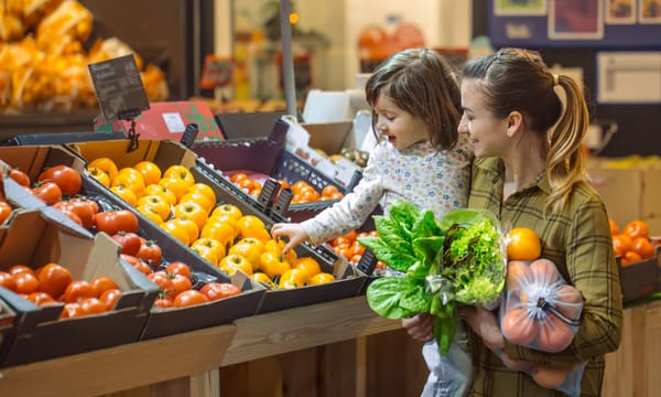 A happy mother buying fresh produce with her toddler.