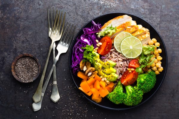 Buddha bowl dish with chicken fillet, brown rice, avocado, pepper, tomato, broccoli, red cabbage, chickpea, fresh lettuce salad, pine nuts and walnuts